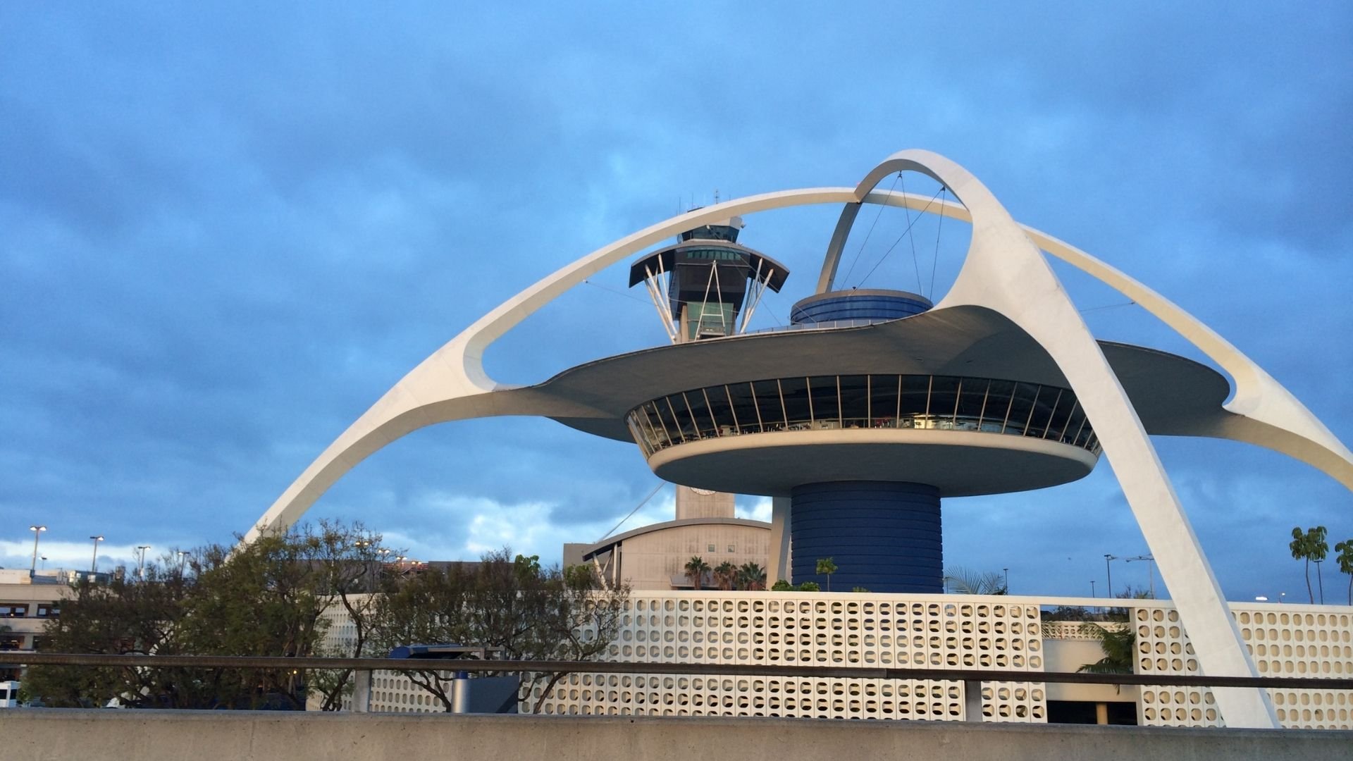 Futuristic white architectural structure with curved arches, observation deck, and control tower against blue sky.