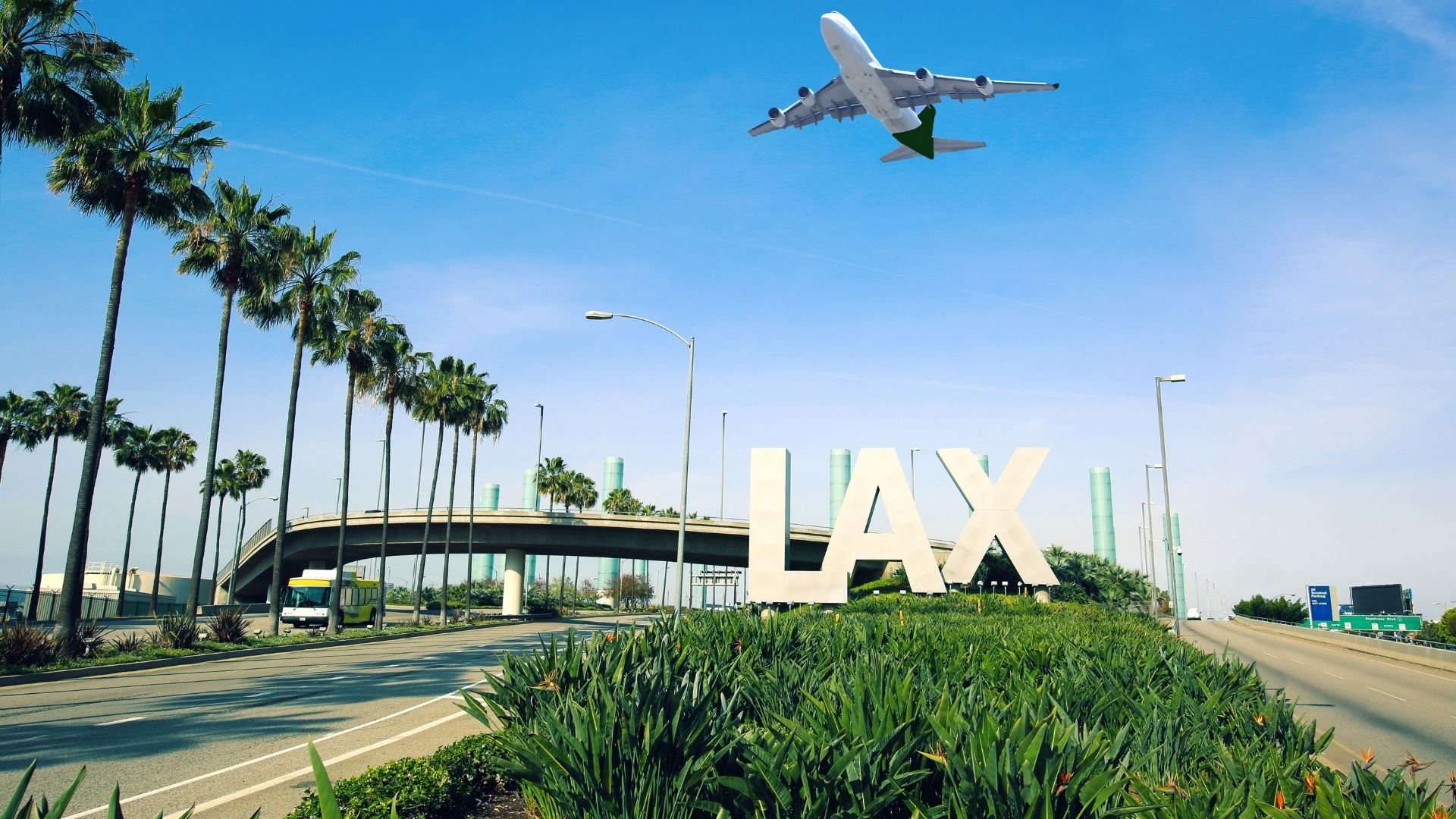 Airplane flying over LAX airport sign with palm trees and blue sky