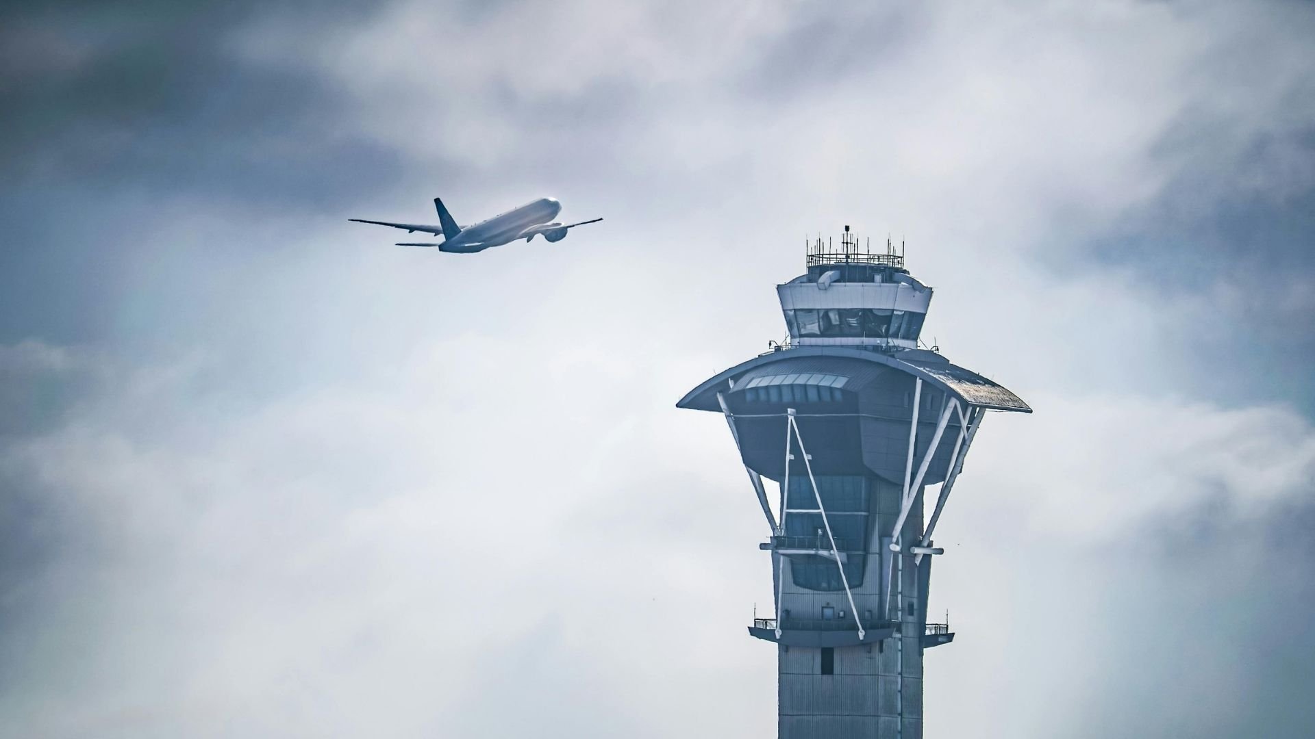 Commercial airplane flying past an air traffic control tower against cloudy sky.